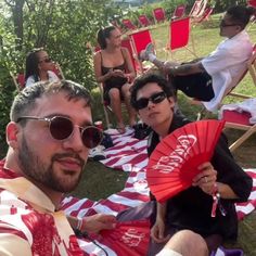 two people sitting on lawn chairs holding red and white fans