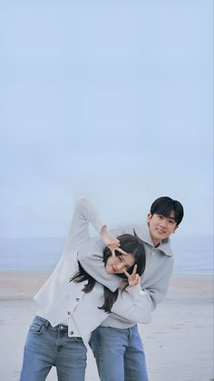 two people standing on the beach with their arms around each other and one person holding his head