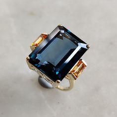 This stunning ring is set in 14k Solid Yellow Gold with Natural London Blue Topaz and Diamond with utmost precision. It is an unique statement gemstone ring for nearly every occasion and is completely hassle-free jewelry. ITEM DETAILS * CENTER GEM: London Blue topaz * GEM SIZE: 13X18mm * GEM SHAPE: Octagon * Gem weight: 18.90 carats * SIDE GEM: Multi Sapphire * GEM SIZE: 3X6 mm * GEM SHAPE: Baugette * Gem weight: 0.90 carats * Total Gem weight: 17.80 carats * Gold Purity: 14KT * Gold Weight: 3.80 gram * Total Weight of the Ring: 7.36 gram The Gold purity is guaranteed and it comes with authentic 14KT gold hallmark. Since my items are handmade, they are absolutely nickel and lead free. CUSTOMIZATION: * Size Customization is available for this ring and it is available in all ring sizes. Kind Orange Sapphire Ring, Sapphire Ring Engagement, Wide Gold Ring, Engagement Ring Sapphire, Sapphire Gem, Statement Rings Diamond, Handmade Jewelry Box, Ring Sapphire, Multi Sapphire