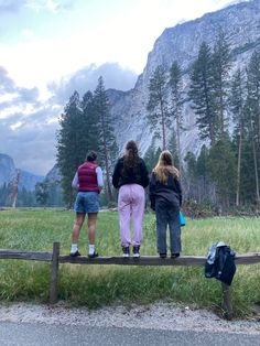 three people standing on a bench looking at the mountains