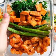 a person holding up a glass container filled with shrimp and veggies on top of it