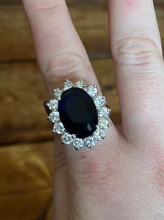 a woman's hand with a ring on it that has an oval blue stone surrounded by small white diamonds