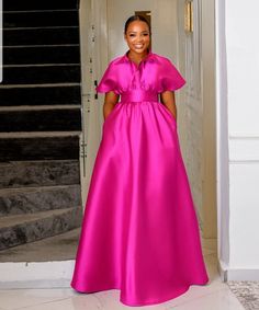 a woman in a bright pink gown stands at the entrance to a white building with stairs