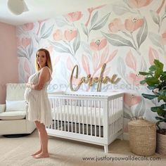 a woman standing next to a baby crib in front of a floral wallpaper