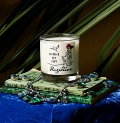 a candle sitting on top of a green book next to a blue cloth and plant