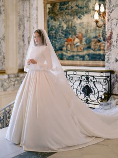 a woman in a white wedding dress and veil standing on a balcony with an ornate painting behind her