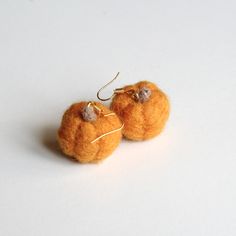 two small oranges are hanging from gold earwires on a white table top