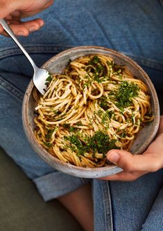 a person is holding a bowl of pasta with parsley on top and a fork in it