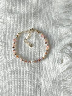 a beaded bracelet on top of a white cloth with gold beads and a tiny charm