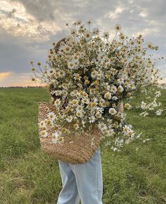 a person standing in a field holding a basket with daisies on it and looking at the sky