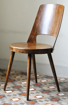 a wooden chair sitting on top of a floor next to a white wall and tiled floor