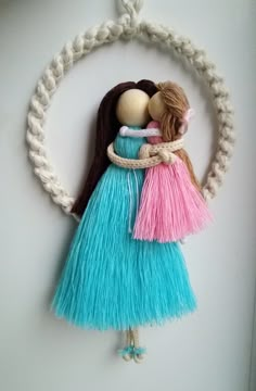 an image of two dolls hanging on the side of a white wall with blue and pink yarn