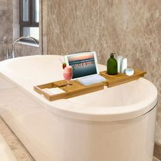 a bath tub with a wooden tray attached to the side holding a laptop and other items