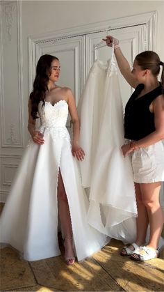 two women standing next to each other in front of a white wall holding up dresses