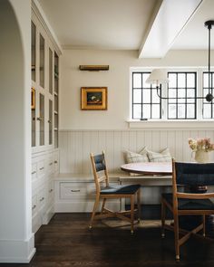 a dining room table with two chairs and a bench in front of the window, next to a built - in bookshelf