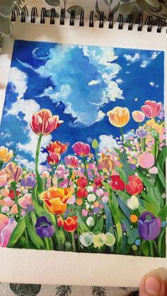 someone is holding up a drawing with flowers in the foreground and clouds in the background