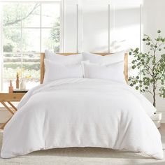 a bed with white sheets and pillows next to a potted plant on a table