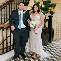 a man and woman standing next to each other in front of a stair case holding bouquets