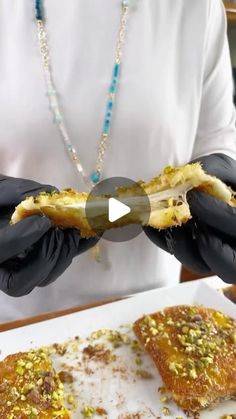 a person in black gloves holding food on top of a white plate with other foods