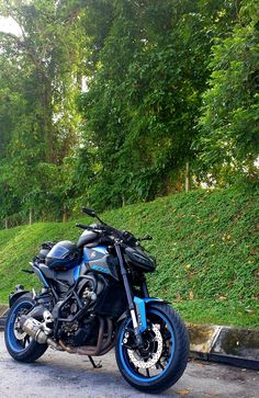 a blue and black motorcycle parked on the side of a road in front of some trees