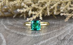 an emerald colored ring sitting on top of a wooden table next to some pine branches