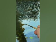 a person is holding a paintbrush in their hand and painting the water with it's reflection