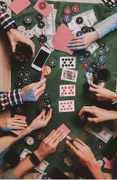 people playing cards at a table with their hands on top of each other and some chips in front of them