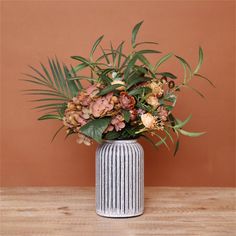 a vase filled with lots of flowers sitting on top of a wooden table next to a brown wall