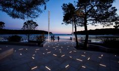 two people are walking down the path by the water at night with lights on them