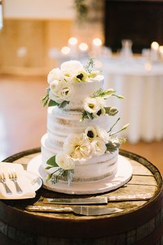 a wedding cake with white flowers and greenery sits on top of a wine barrel