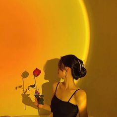 a woman holding a rose in front of a yellow and orange wall with the shadow of a sun behind her