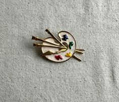 You will receive this pretty vintage artist paltette brooch.  It measures 2 3/8" x 1 1/2" and has a colorful enamel front.  The brooch is cast in a gold tone base metal and it is unbranded.  This brooch is in good preowned wearable condition with minimal signs of wear. We have rebranded, and since December 2023 we are Lazy Frog Thrifters.  We have been flipping high end home decor that we find at thrift stores, yard sales, flea markets, and estate sales.  Come check out the old and tired items that we have given a French Country look or Cottage Core vibe to at:  https://lazyfrogthrifters.etsy.com Artistic Enamel Brooch Pin For Gift, Multicolor Enamel Collectible Pin, Mid-century Gold Enamel Jewelry, Gold Enamel Lapel Pin, Handmade Artistic Gold Brooch, Unique Handmade Gold Enamel Pin, Vintage Multicolor Enamel Brooch Pin, Collectible Gold Enamel Pins, Retro Gold Collectible Pins