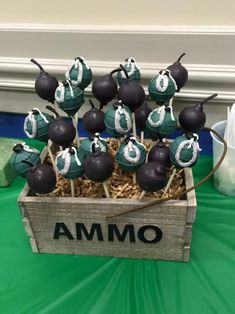 a wooden crate filled with cake pops covered in green and black frosting sitting on top of a table