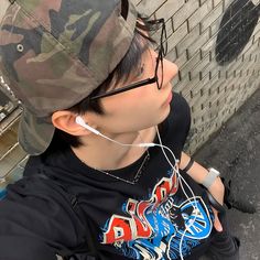 a young man wearing headphones while leaning against a brick wall