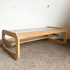 a wooden and glass coffee table on carpeted floor with white wall in the background