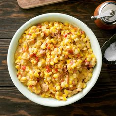 a white bowl filled with corn on top of a wooden table next to two spoons