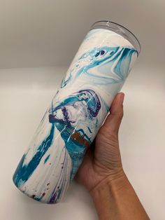 a hand holding a blue and white tumbler cup with an artistic design on it