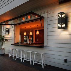 an outdoor bar with stools and lights on the side of a white house at night