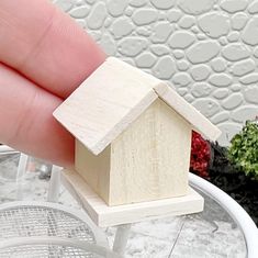 a small wooden house sitting on top of a white table next to some potted plants