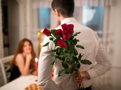 a man holding a bouquet of roses in front of a woman sitting at a table