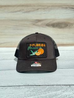 Florida Flavor: Orange Grove Black Hat Black Six-panel Trucker Hat With Logo Patch, Black Trucker Hat Six-panel, Urban Black Trucker Hat With Logo Patch, Black Urban Trucker Hat With Logo Patch, Black Six-panel Snapback Hat With Logo Patch, Black Trucker Hat With Logo Patch For Outdoor, Black Six-panel Trucker Hat Urban Style, Urban Black Six-panel Trucker Hat, Orange Grove