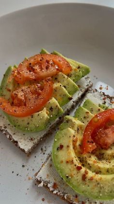 two slices of avocado on toast with tomatoes and seasoning sprinkles