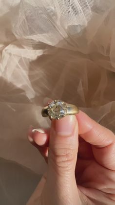 a hand holding a ring with a diamond in it's middle, on top of a sheet of plastic