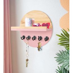 a pink shelf with keys and sunglasses hanging from it's sides, next to a potted plant