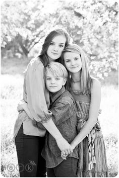 black and white photograph of three girls hugging each other in front of a field with trees