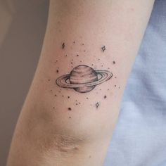 a small saturn tattoo on the right arm and shoulder, with stars around it in black ink