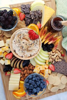 an assortment of cheeses, crackers, fruit and nuts on a cutting board