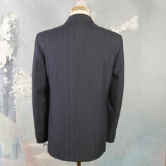 "This navy blue double-breasted blazer has notch lapels and padded shoulders, and closes in the front with one button (four in total show on the front). Three buttons decorate each sleeve cuff. The dark blue wool-blend jacket has three pockets on the front, and is fully lined in a navy blue satin viscose fabric (with two inner pockets). The fabric has a double pinstripe pattern, with a textured chevron herringbone running vertically as well. Brand label: Turo (Made in Finland) Size: 40 US/UK Mat Striped Notch Lapel Blazer With Double Button Closure, Striped Blazer With Double Button Closure And Notch Lapel, Double-breasted Pinstripe Fitted Blazer, Striped Double Breasted Suit With Notch Lapel, Fitted Pinstripe Double-breasted Blazer, Striped Blazer With Double Button Closure For Tailoring, Fitted Pinstripe Outerwear For Semi-formal Occasions, Double-breasted Pinstripe Blazer For Formal Occasions, Formal Pinstripe Double-breasted Blazer