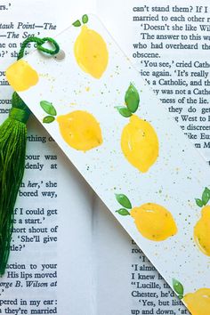 a bookmark with lemons and green tassel on top of an open book