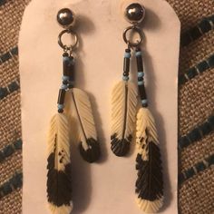 two pairs of earrings with feathers hanging from them on a piece of white and black paper